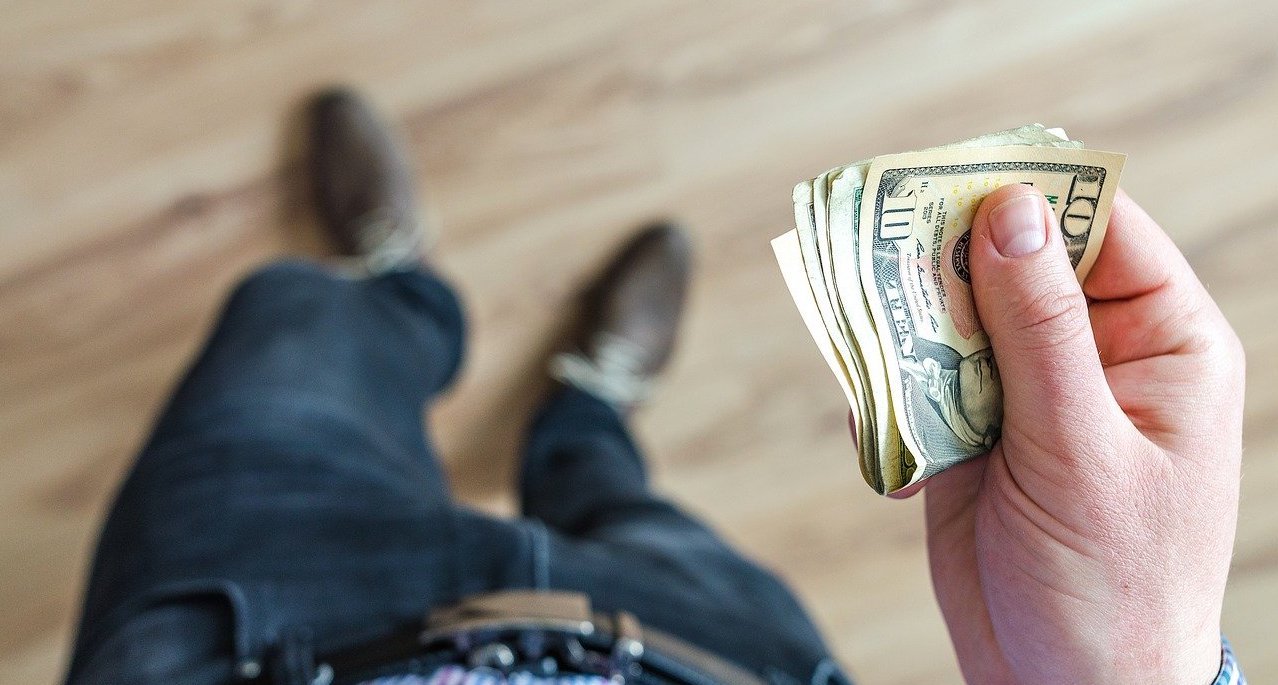 Person holding a few folded dollar bills