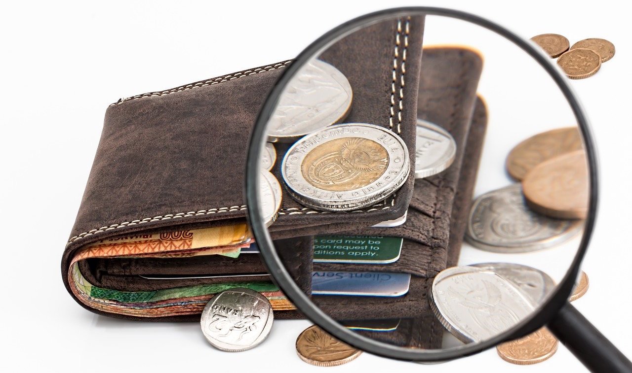 Magnifying glass focusing on coins and a brown wallet