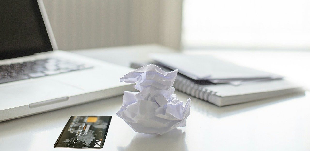 Paper crumpled on a table beside a Visa card and laptop