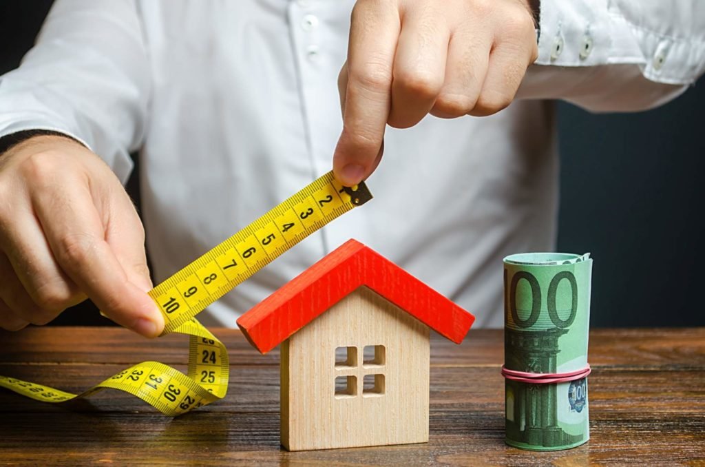 Man measuring a miniature house with a tape measure 