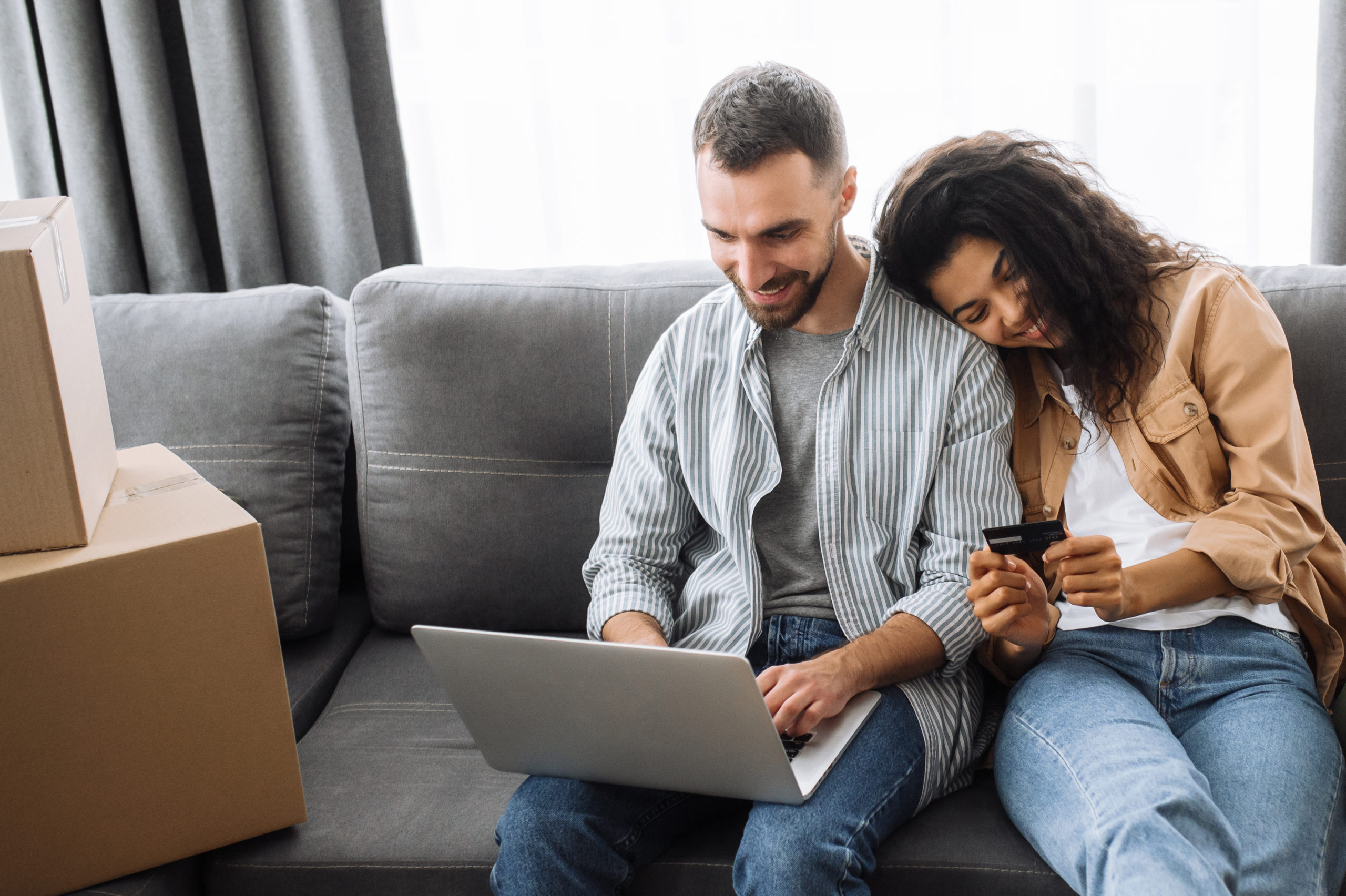 Couple sitting on the couch while the woman is holding a card and her husband is using a laptop
