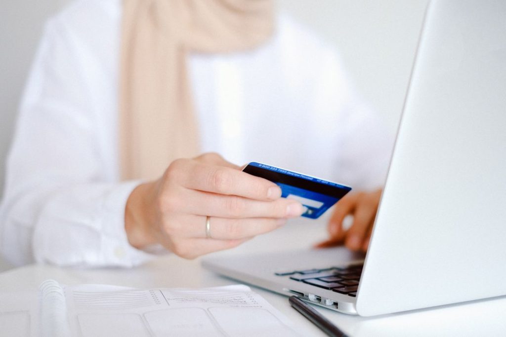 Woman holding a blue credit card while browsing her laptop
