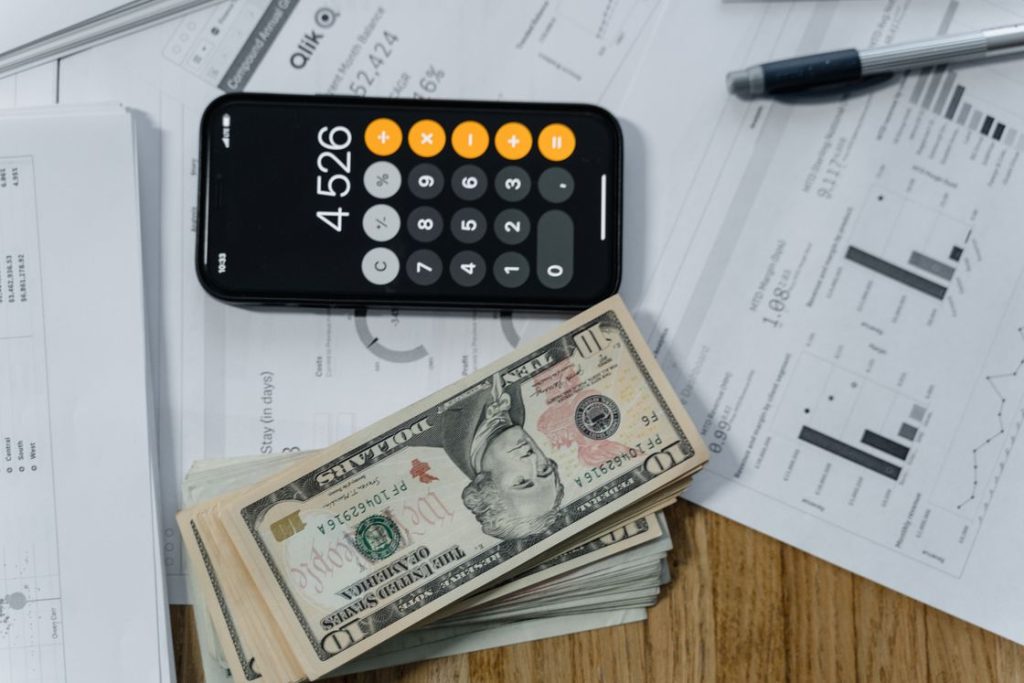 Pile of dollar bills, calculator and printed documents laid out on a table