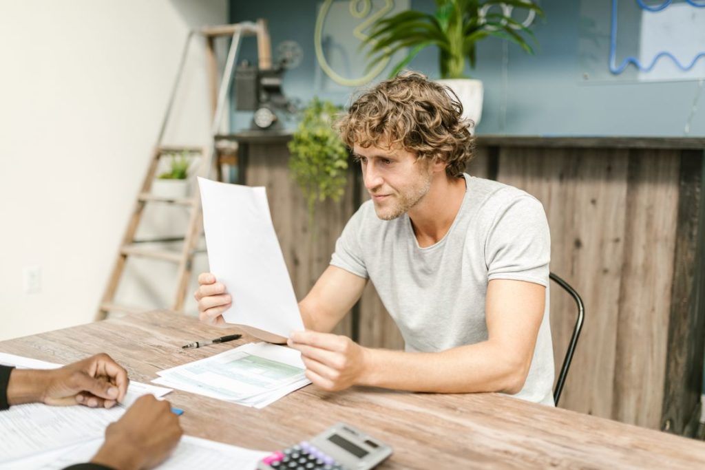 Man looking at a printed document while his friend looks on