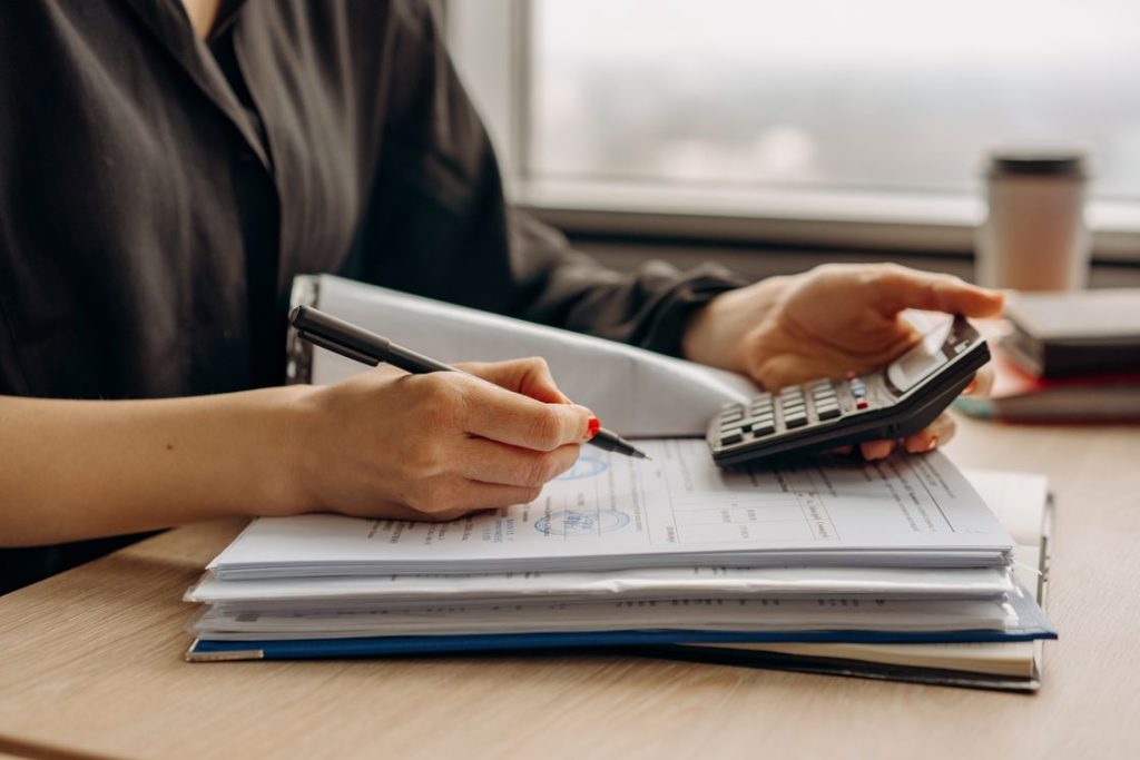 Woman writing notes on a data sheet while looking at a calculator