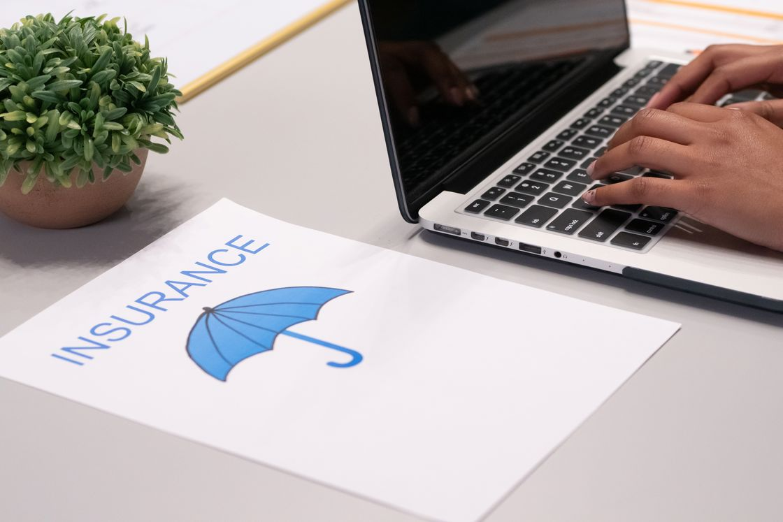 Paper with a printed image of an umbrella and the word "insurance, placed beside a man typing on his laptop