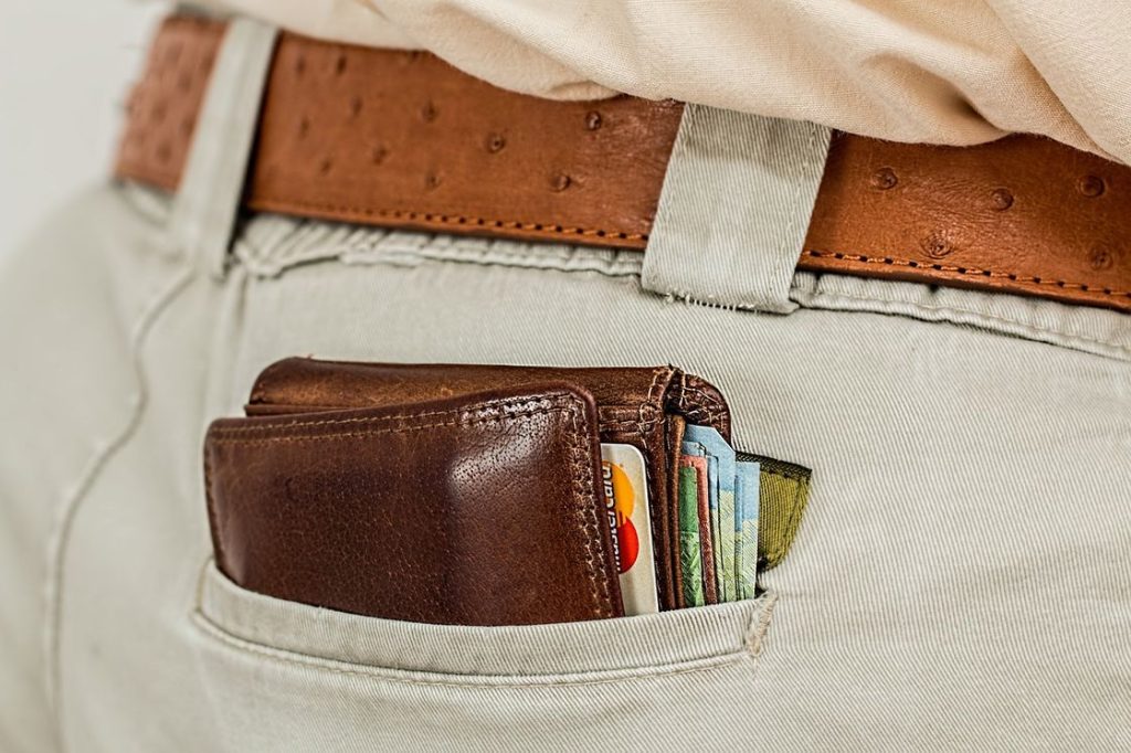 Brown wallet with credit cards, paper bills are visible in the pockets of a man's pants