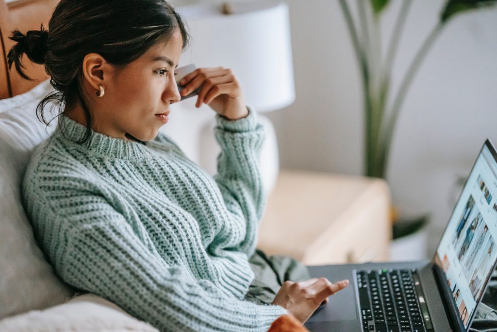 A woman scrolling through her laptop while holding her credit card pointed at her cheeks