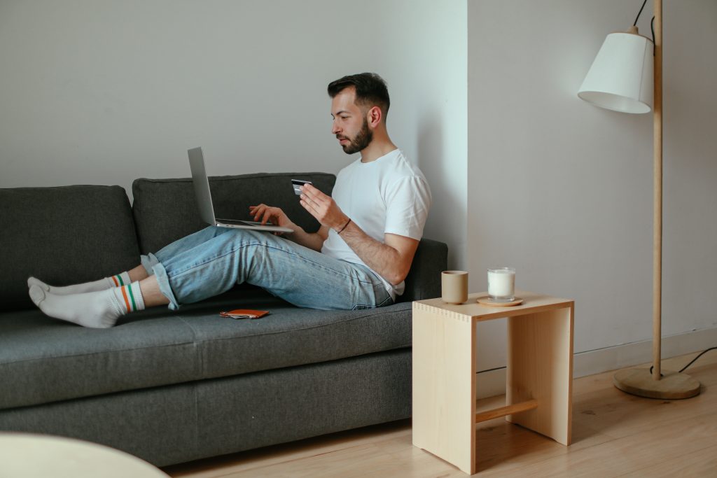 A man sitting on a couch while scrolling through her laptop and holding her credit card