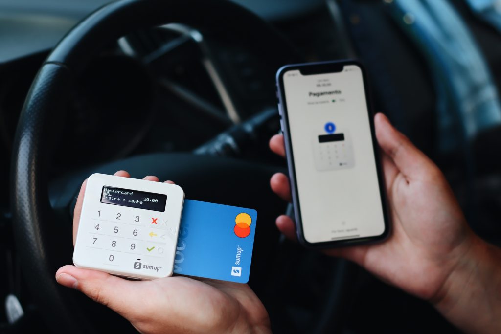 A man holding a credit card with terminal payment and a phone inside the car
