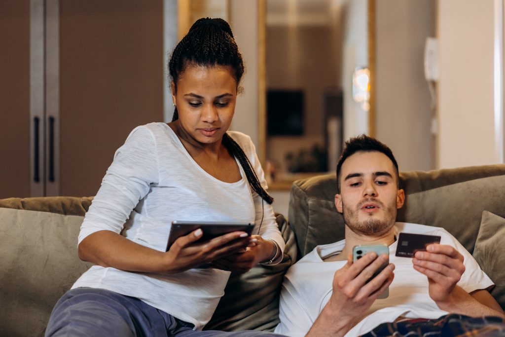 A couple on a couch with the man holding his phone and credit card and his wife holding a tablet