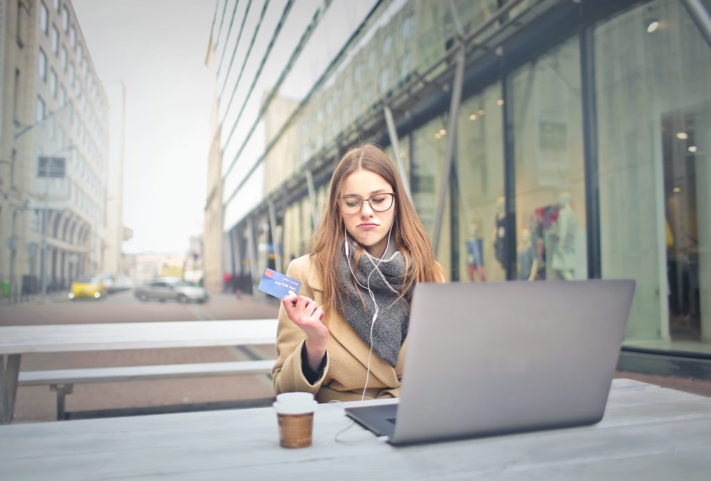 A woman sitting outside holding her credit card with a coffee and a laptop in front of her