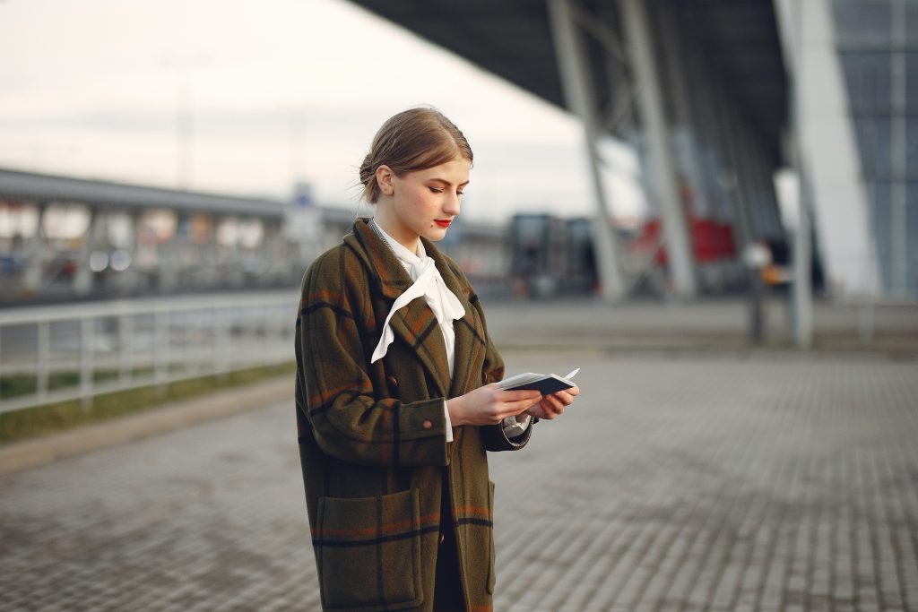 A woman standing outside holding her passport and other travel papers