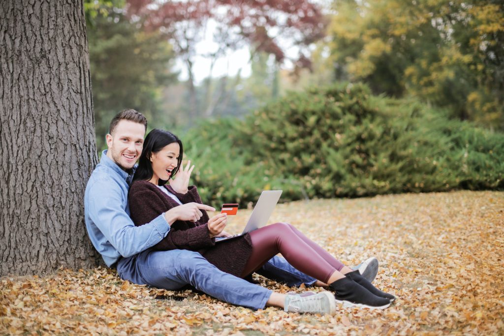 A couple sitting under a tree looking happy with their credit card