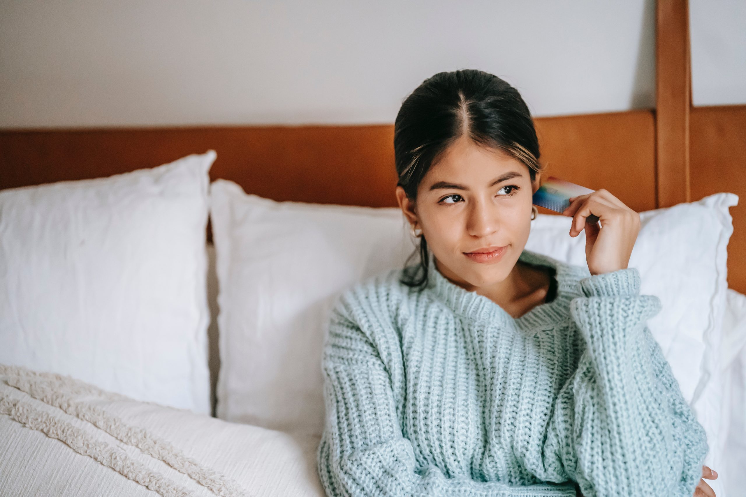 A woman sitting on the bed holding a credit card