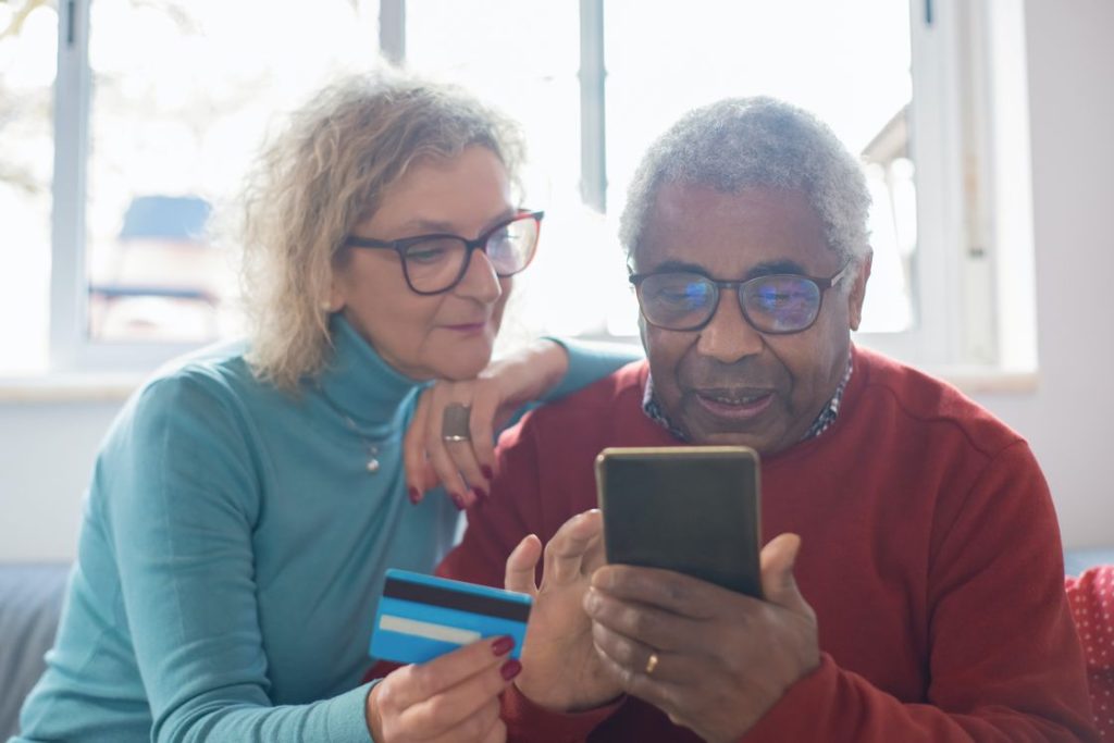 Elderly couple browsing through their phone while the other is holding out a credit card in their hand