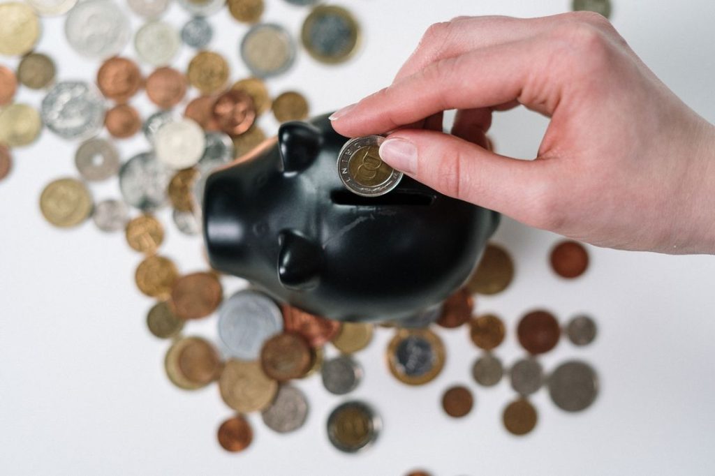 Person putting a coin in a black piggy bank with various coins scattered on the table