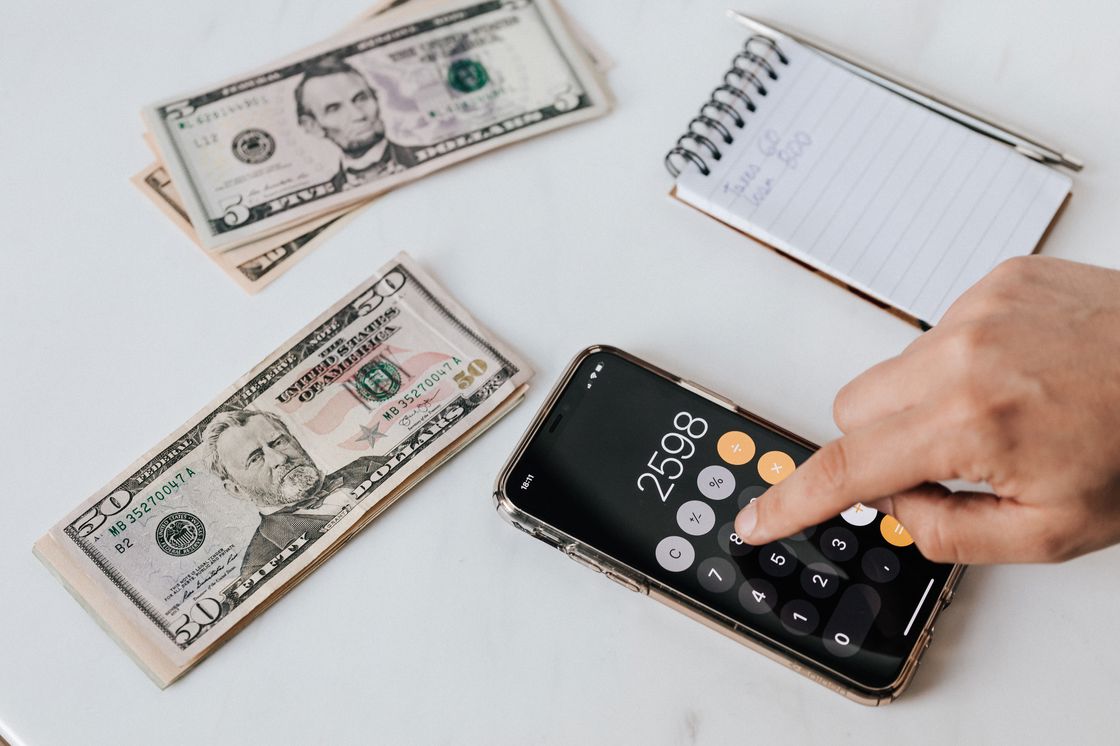 Person using a calculator while dollar bills and a notepad are placed in a table