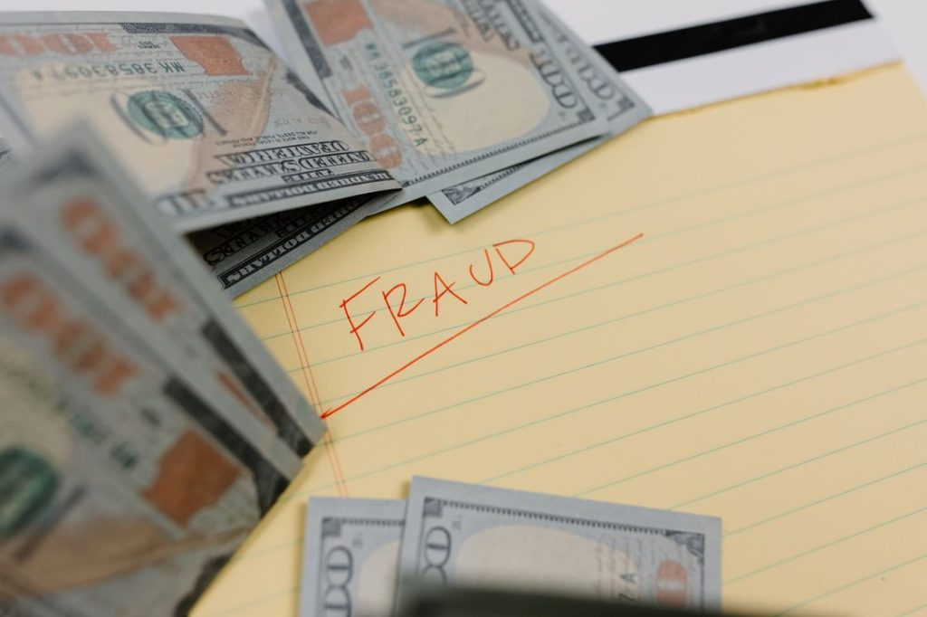 Dollar bills surrounding a yellow pad with a written word "fraud" in the page