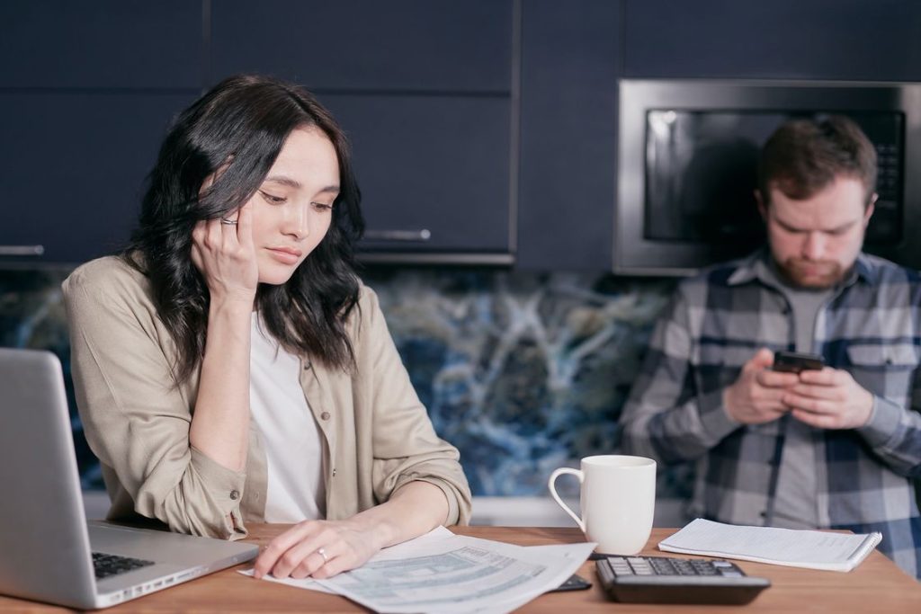 Woman with her hand resting in her chin as she reviews a document while her husband is looking at his phone