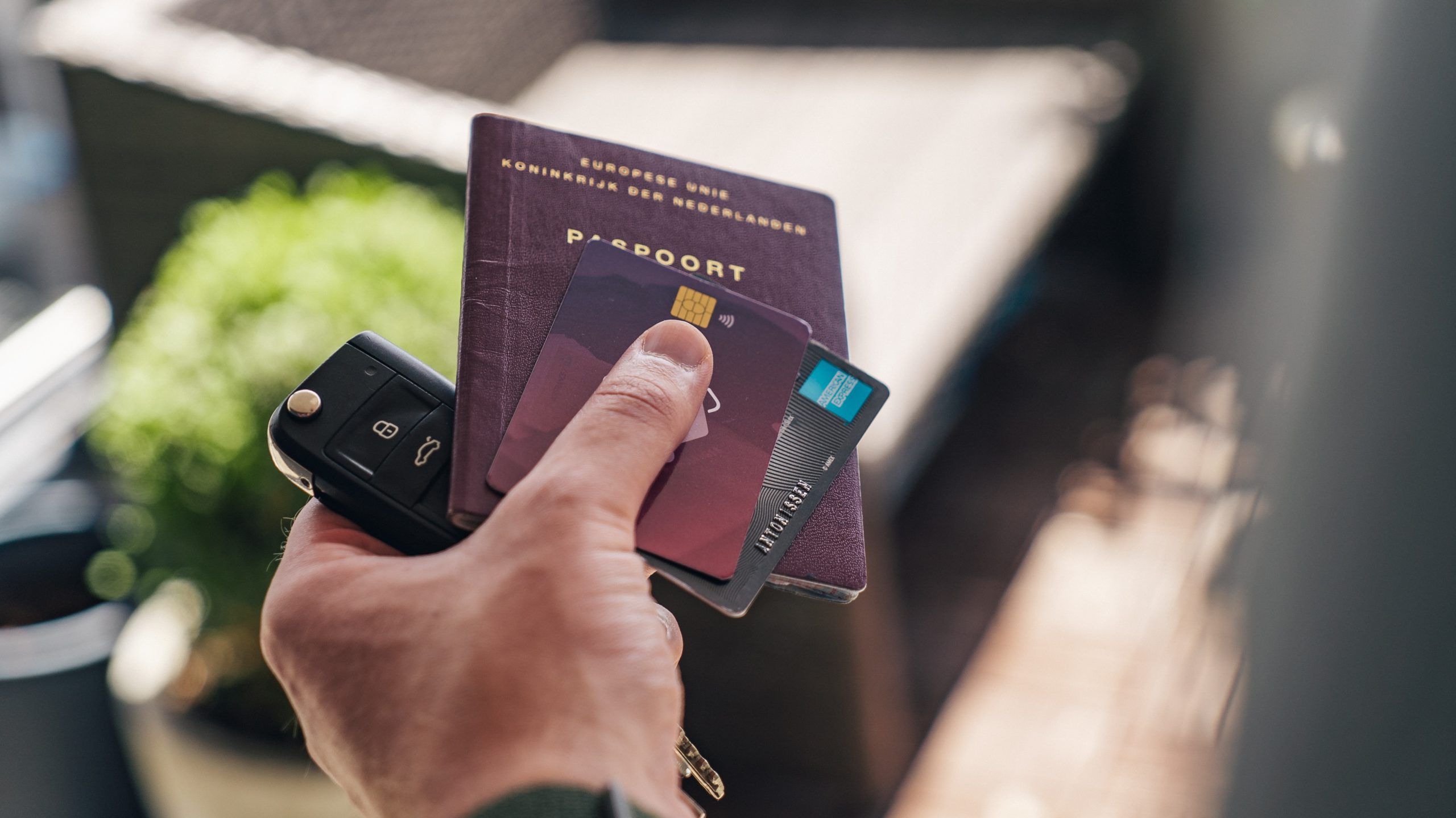 A hand of a man holding a car key, passport, and credit cards