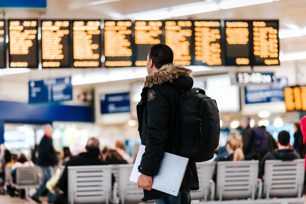 A man holding a laptop and wearing backpack standing at the airport