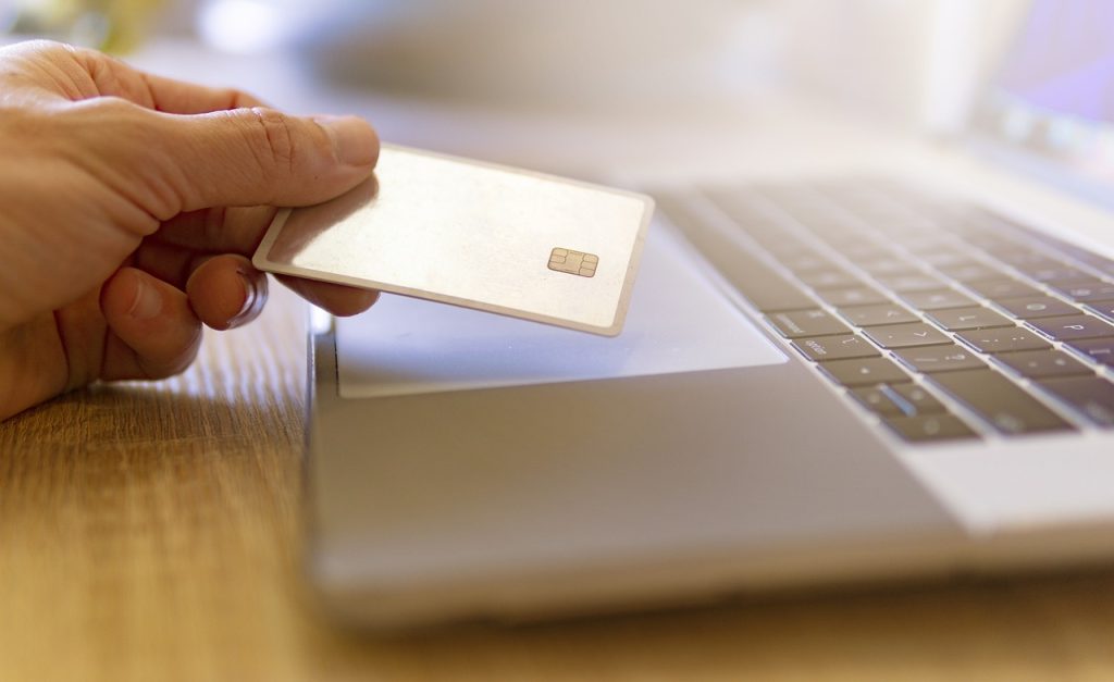 A man holding a credit card in front of a laptop