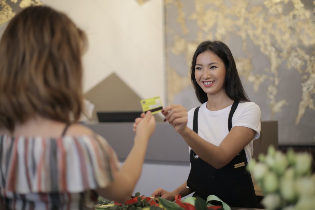 A woman smiling handling the credit card to its owner