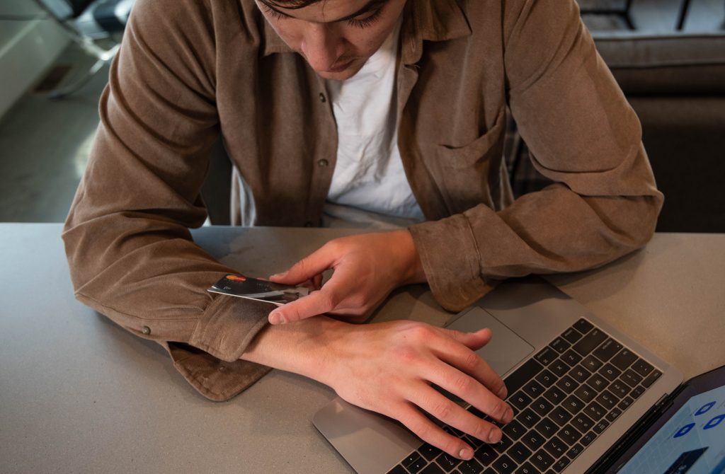 A man looking at his credit card while typing on his laptop
