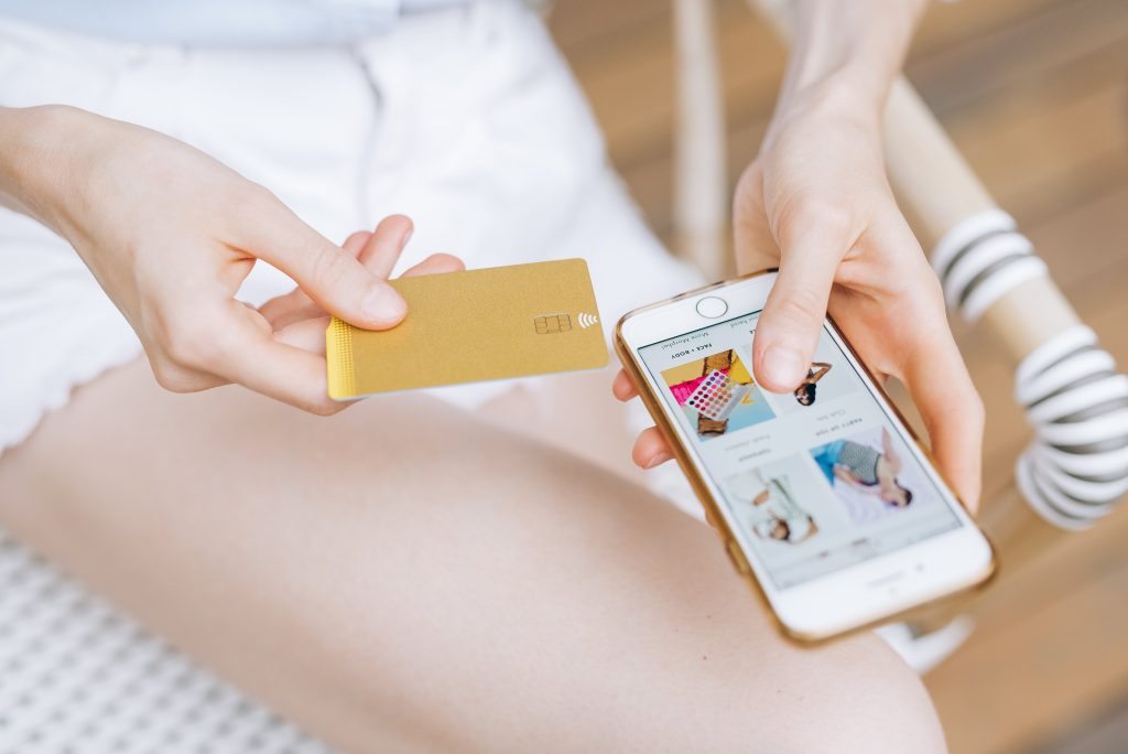 A woman holding a gold credit card while shopping on her smartphone