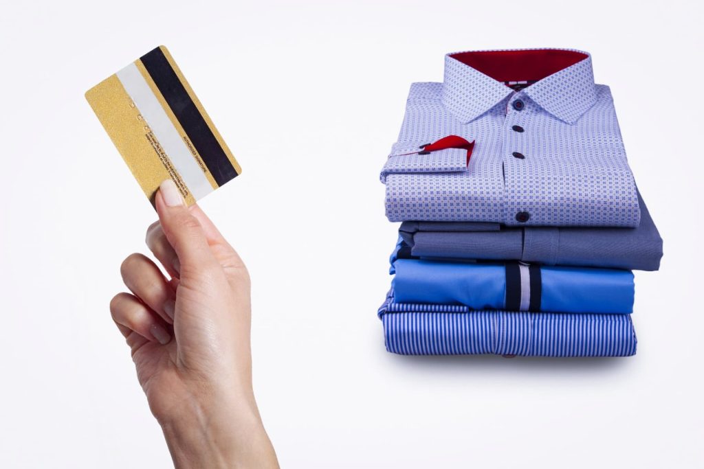 Hand holding a credit card with a pile of shirts in the background