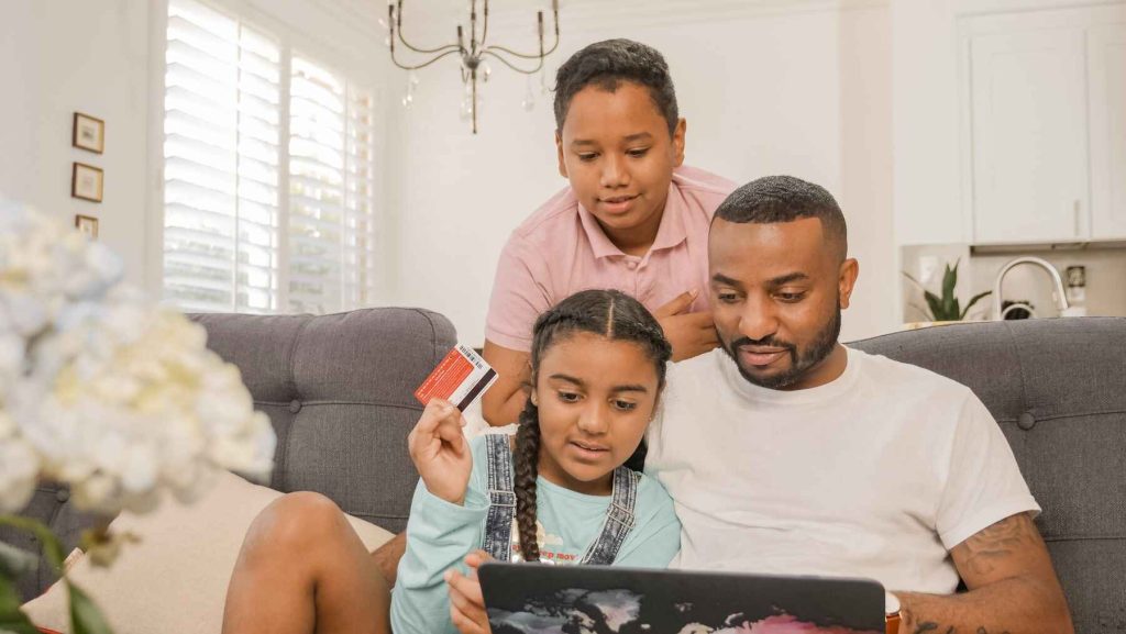 Father browsing his laptop while his daughter is holding credit card and his son looks on