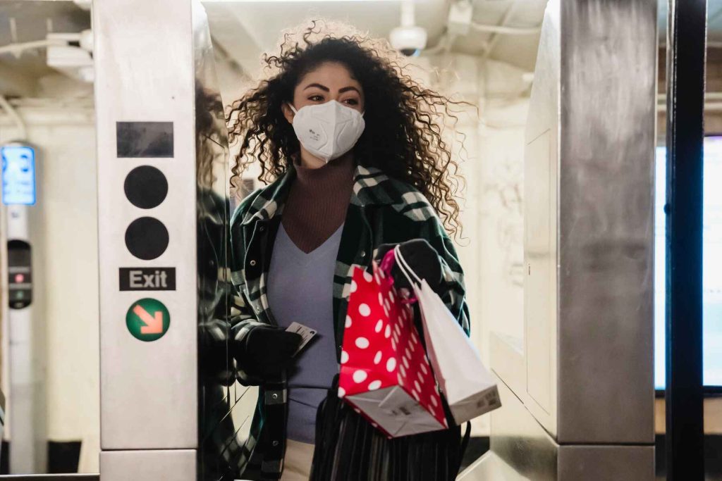 Woman with a white mask holding paper bags as she exits a turnstile in a subway