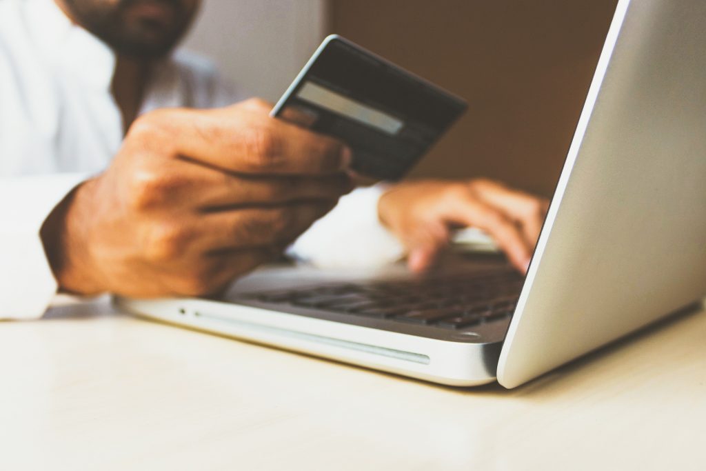 A man holding a credit card while typing on a laptop