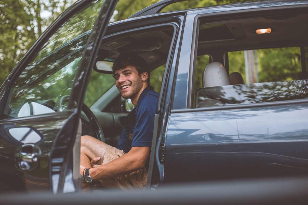 A man sitting and smiling on the driver seat with his door open