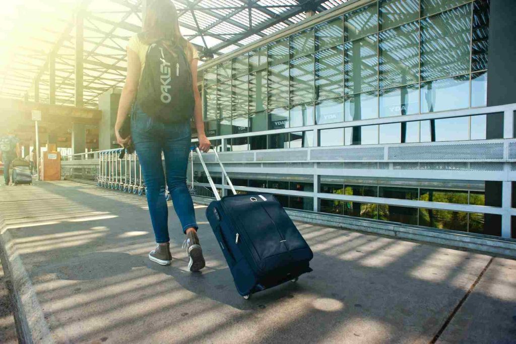 A woman holding a rolling suitcase with a backpack and a pouch at the airport