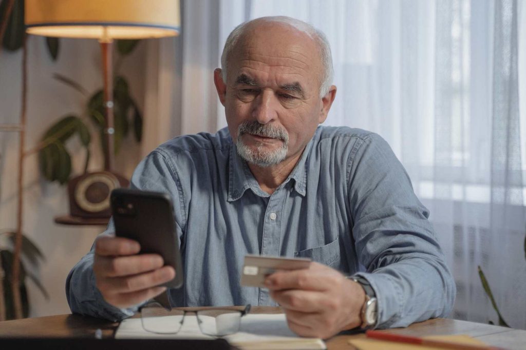 An old man holding his phone and a credit card