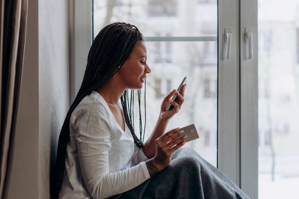 A woman smiling on her phone while holding her card on the other hand