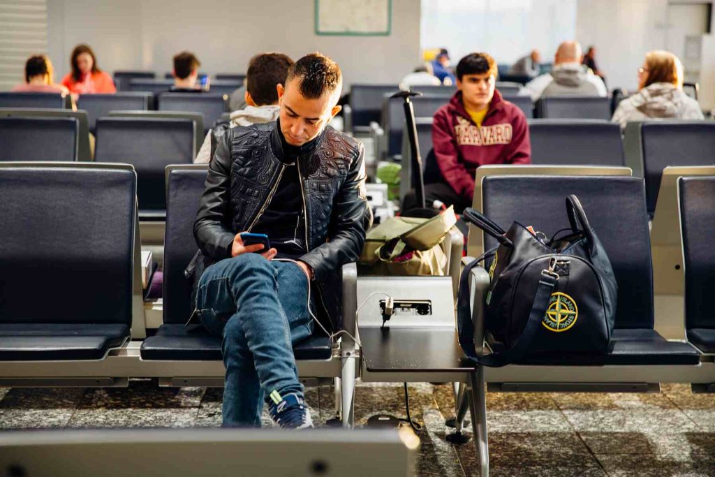 A man sitting and charging his phone on the airport's lobby