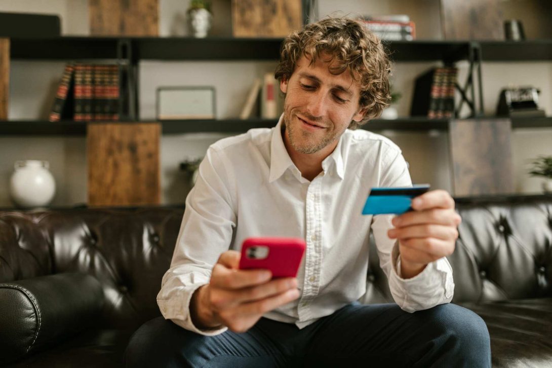 A man smiling while holding his credit card and looking at his phone