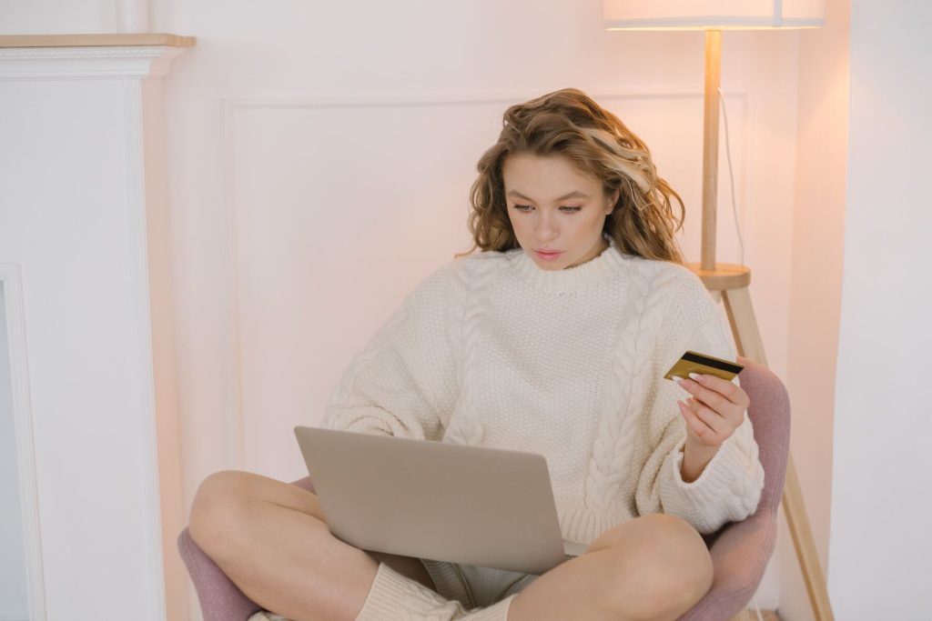 A woman holding her card while typing on her laptop