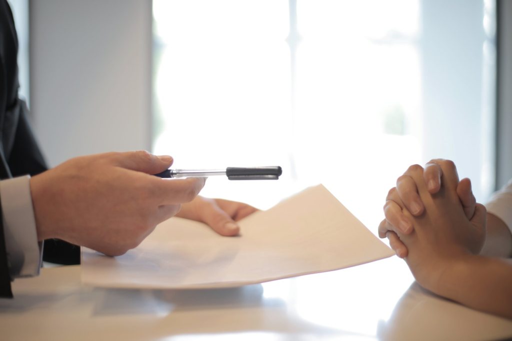 A man handling a pen and paper to a woman on the other side of the table