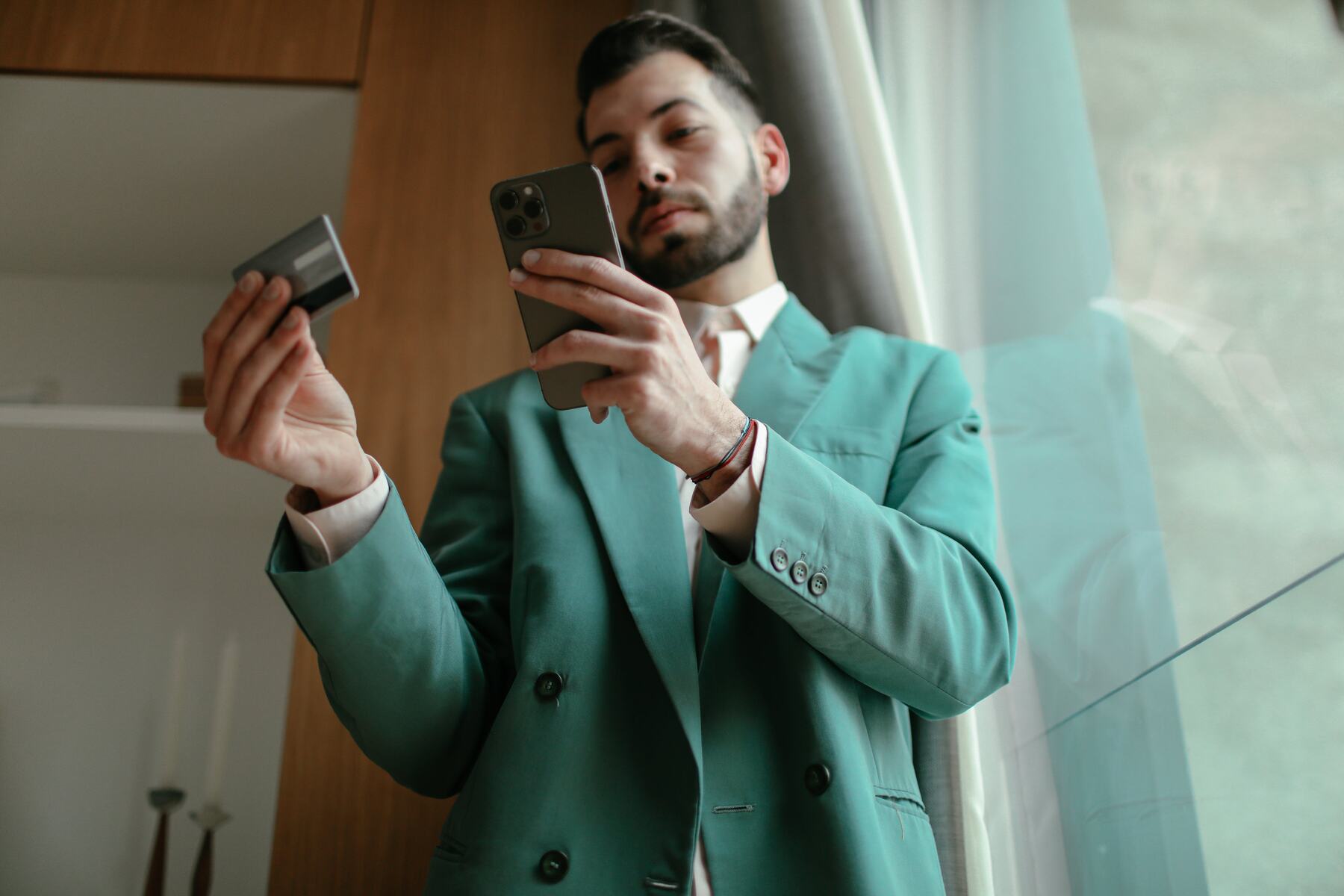 A man wearing formal green suit holding his mobile phone and credit card