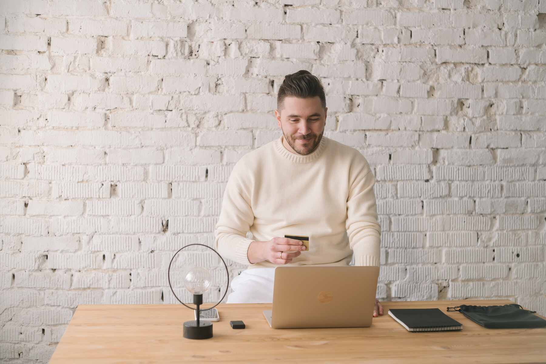 A man smiling while looking at his laptop and holding his credit card