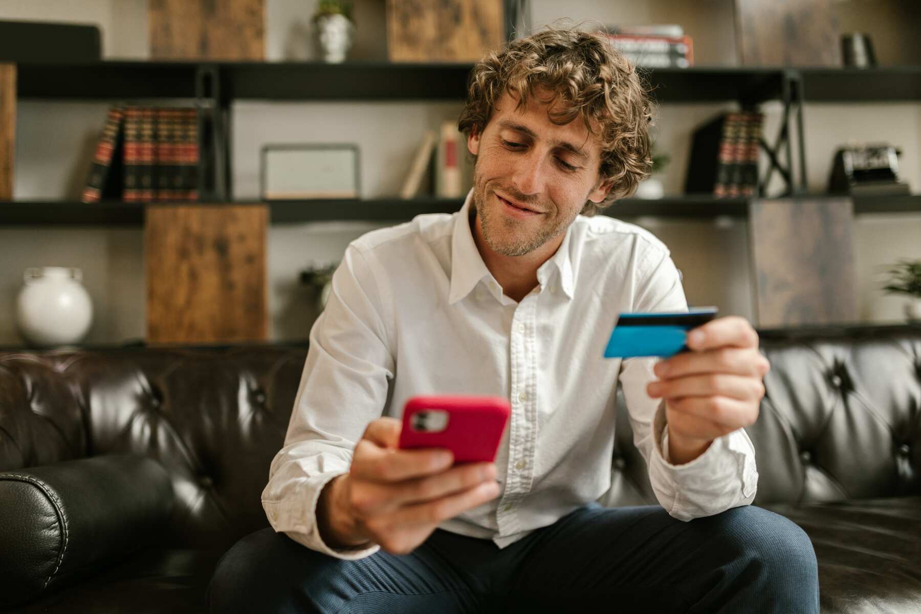 A man holding his blue credit card and mobile phone while smiling