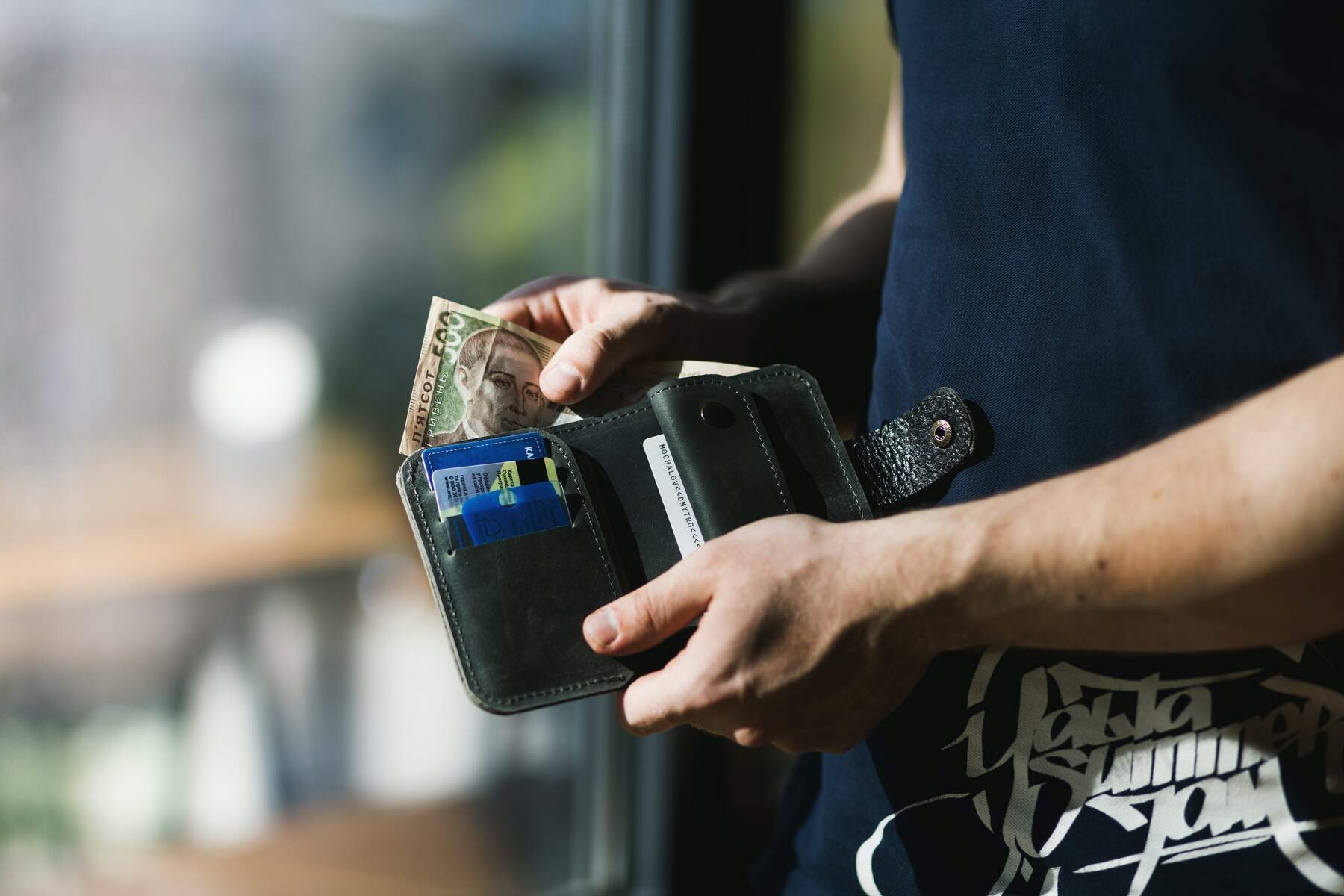 A man getting money on her black wallet with some cards in it