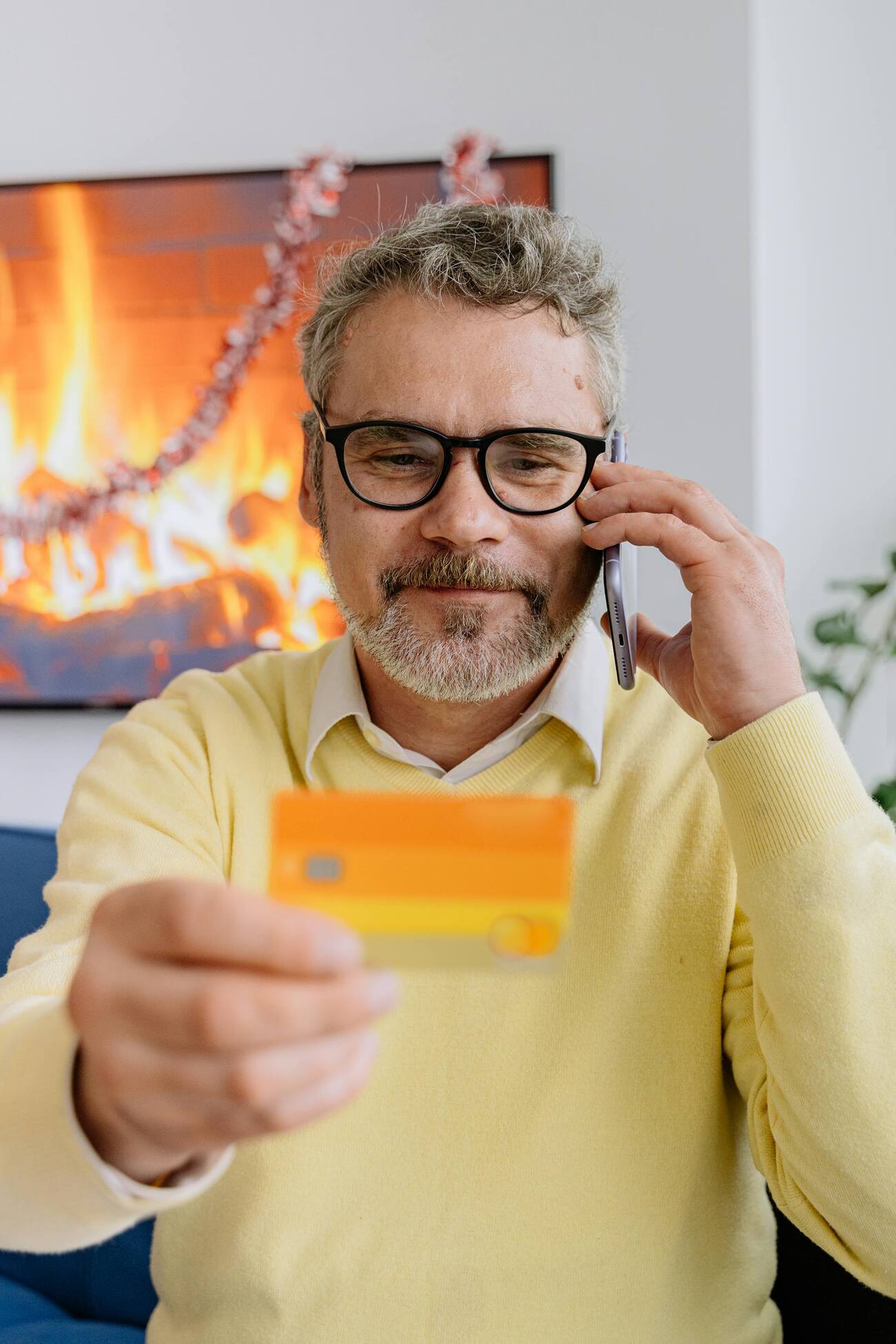 A man holding a credit card and talking on the phone, with a digital fireplace in the background