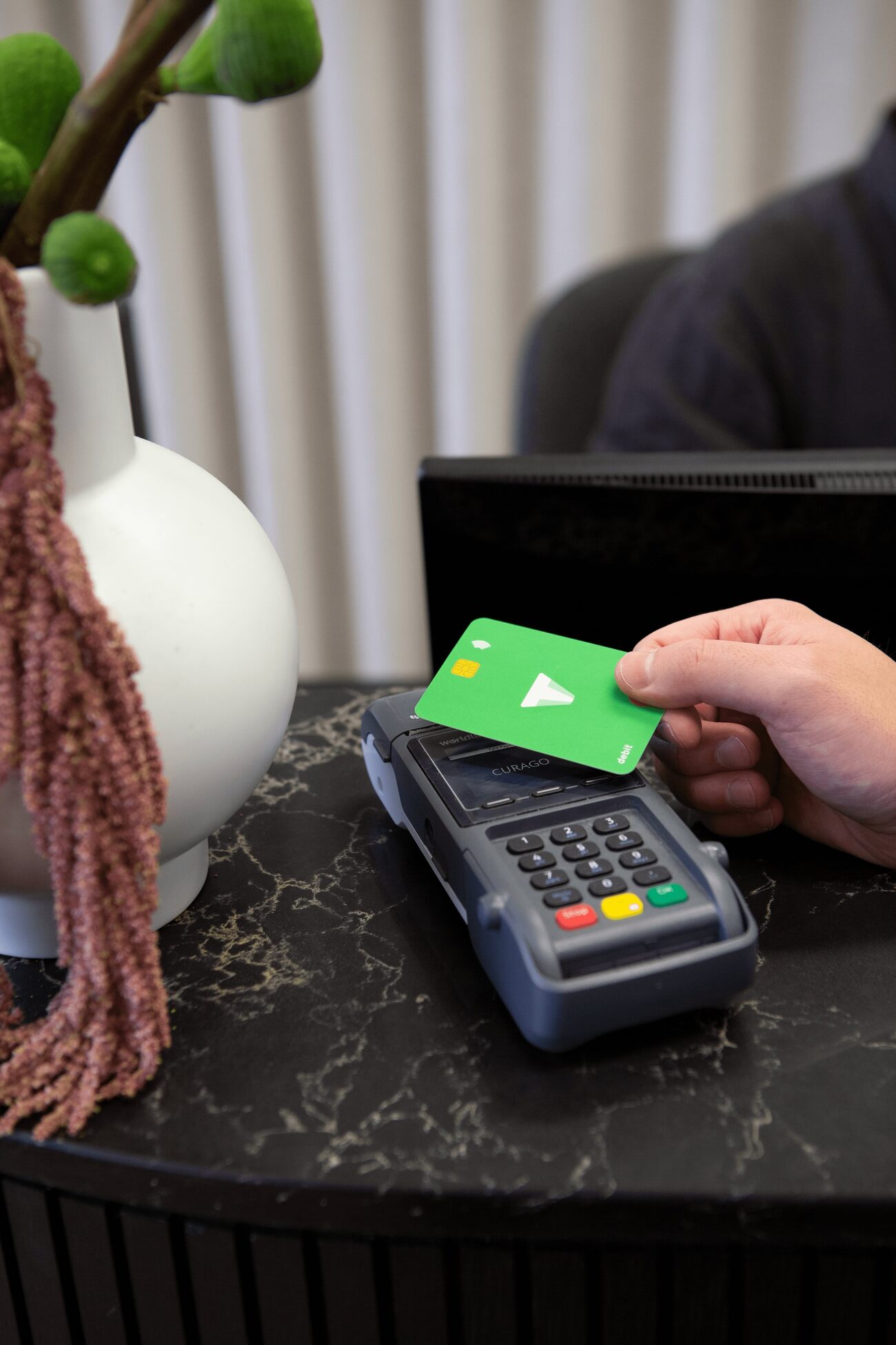 A person's hand holding a credit card near a payment terminal