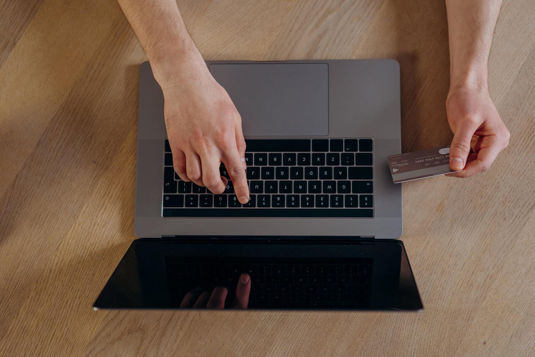 A man's hands holding a credit card and typing on a laptop