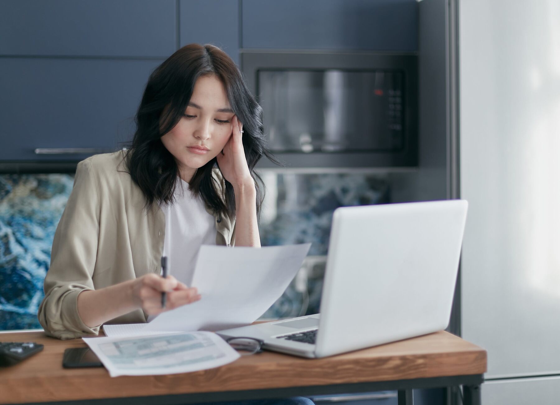 Woman looking at a printed document while working on her laptop